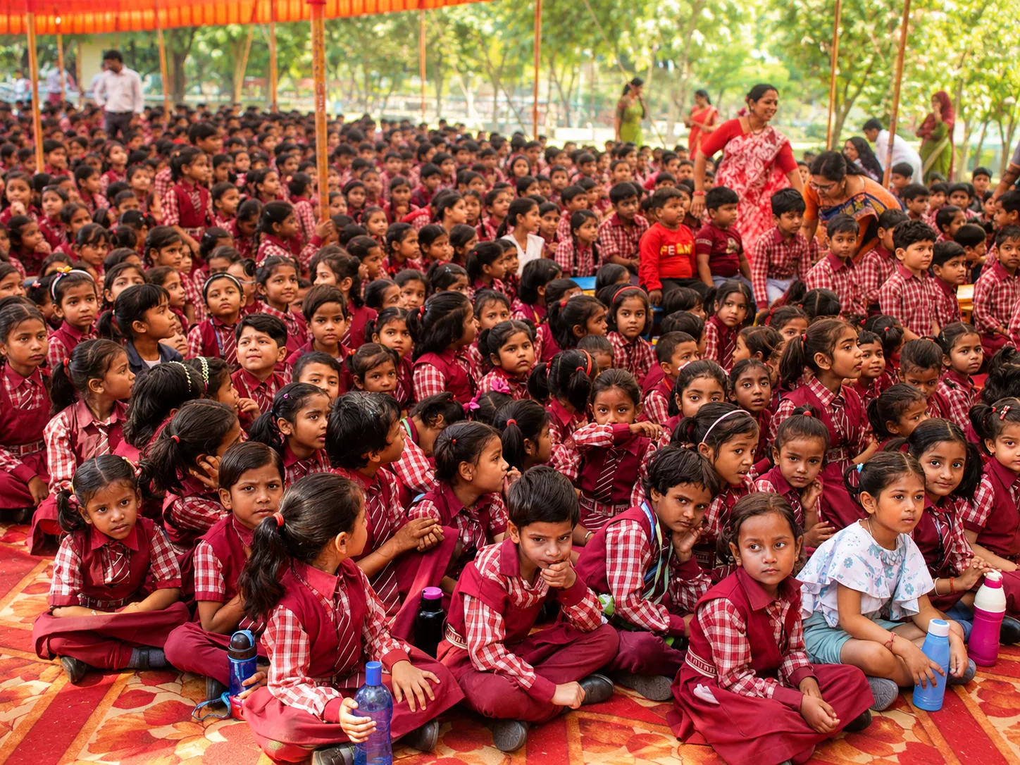 Hundreds of pupils in the maroon check uniform seated under a canopy for a school gathering